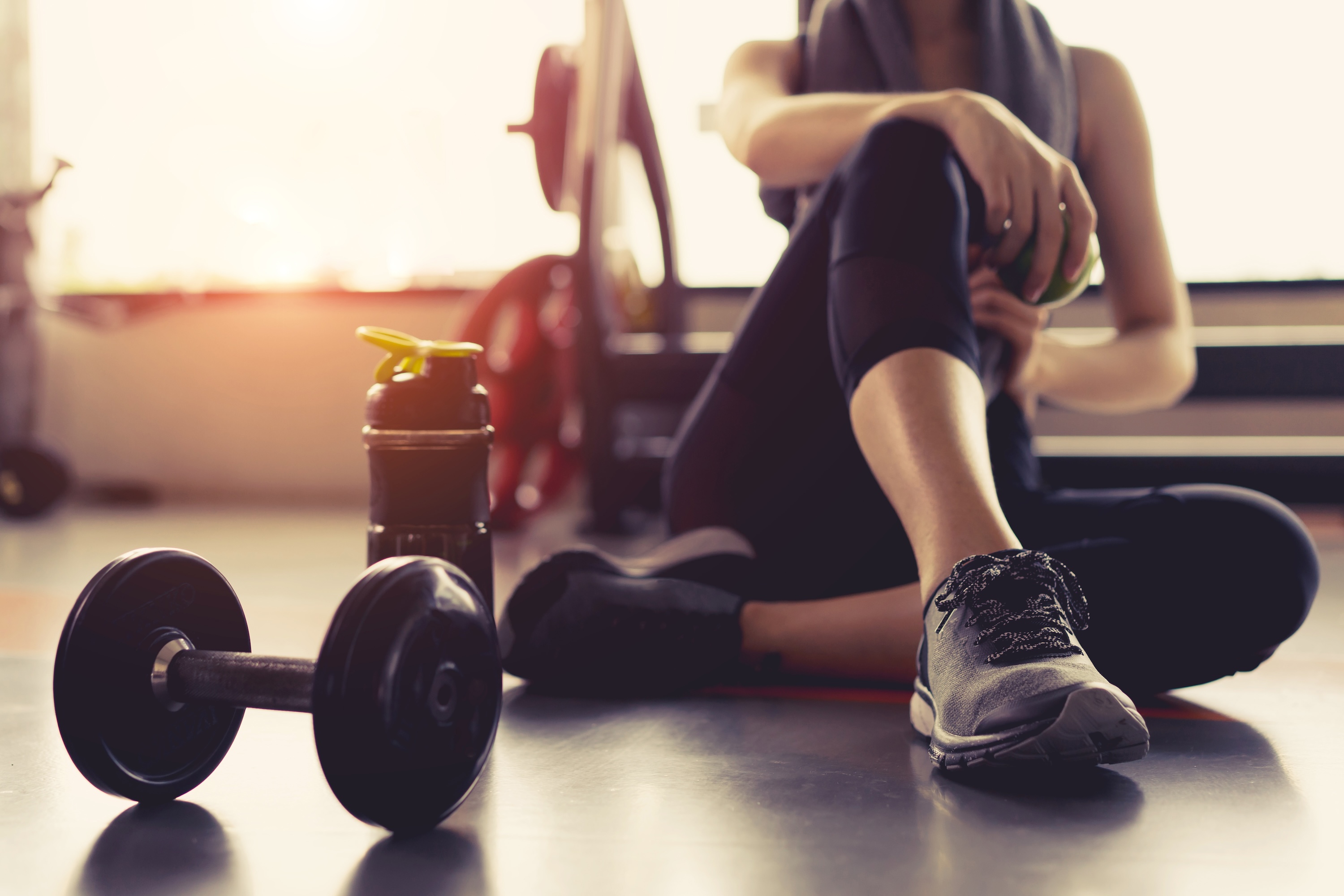 Woman in exercise clothing sits on floor next to dumbells